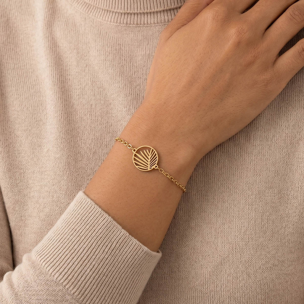 Goldfarbenes Damen Armband mit Palmblätter Anhänger am Handgelenk eines Models getragen.