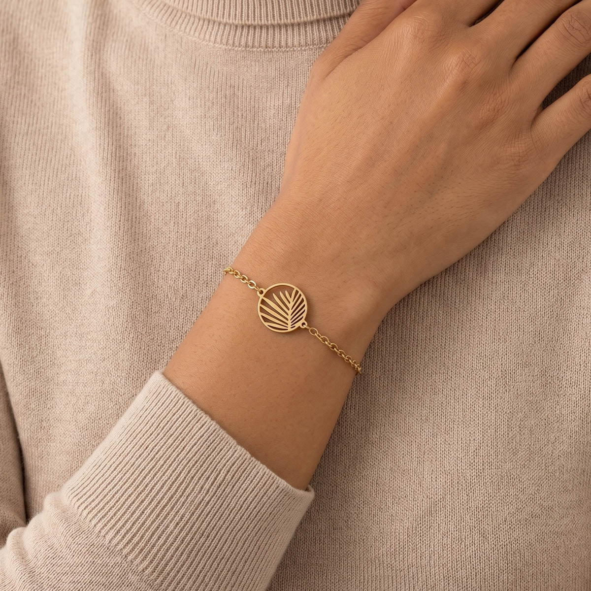 Goldfarbenes Damen Armband mit Palmblätter Anhänger am Handgelenk eines Models getragen.