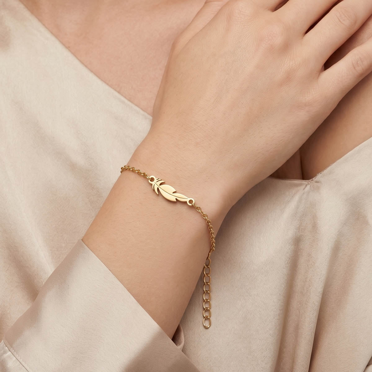 Goldfarbenes Damen Armband mit Feder Anhänger am Handgelenk eines Models getragen.
