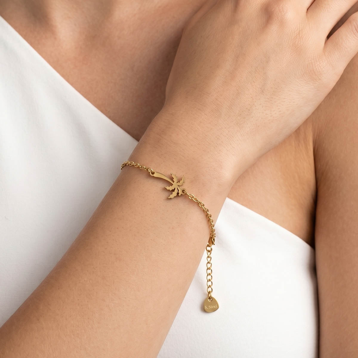 Goldfarbenes Damen Armband mit Palmen Anhänger am Handgelenk eines Models getragen.