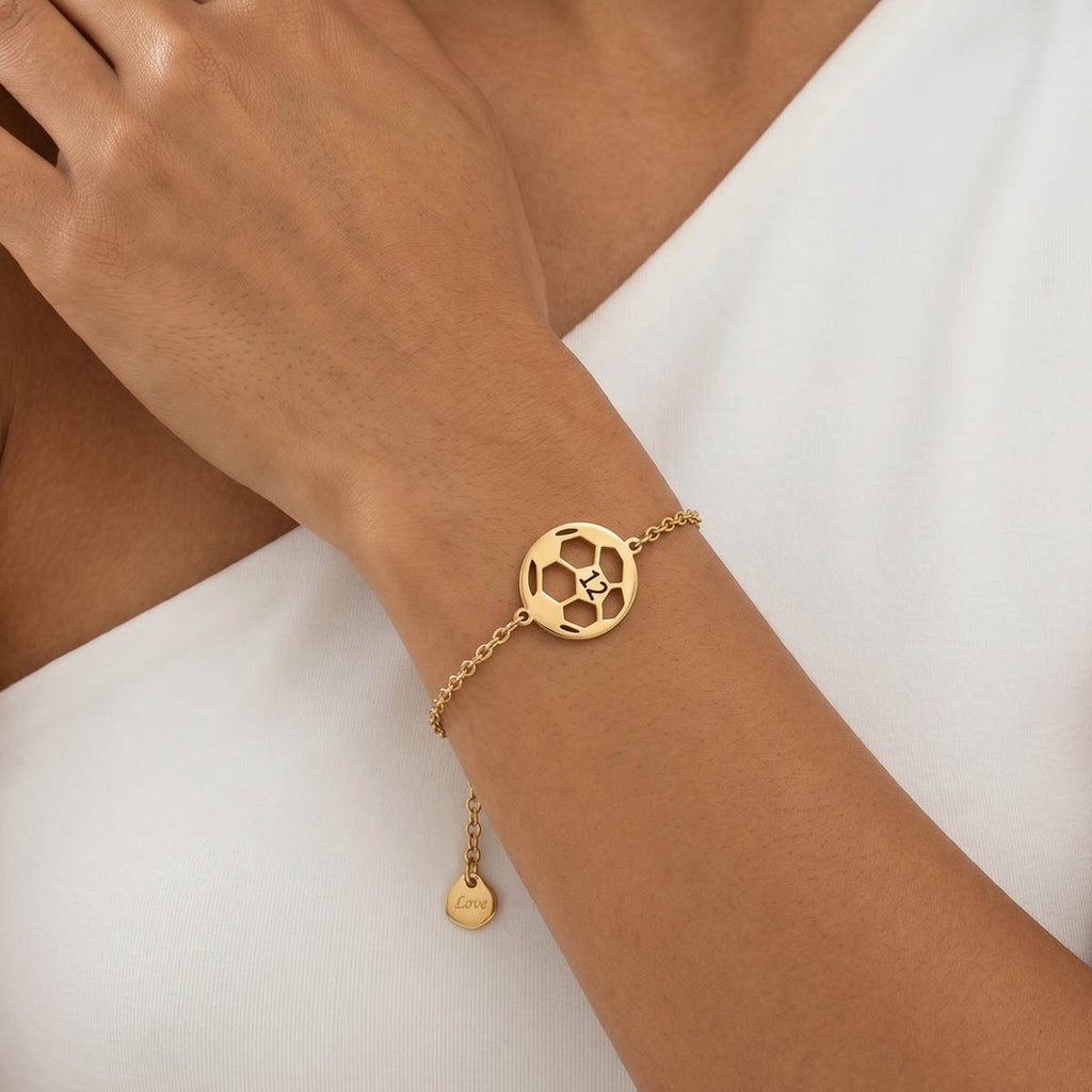 Goldfarbenes Damen Armband mit Fußball Anhänger am Handgelenk eines Models getragen.