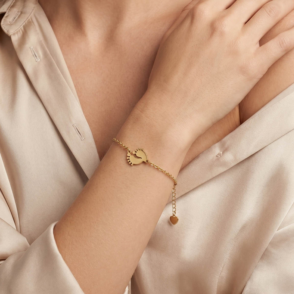 Goldfarbenes Damen Armband mit Babyfüße Anhänger am Handgelenk eines Models getragen.