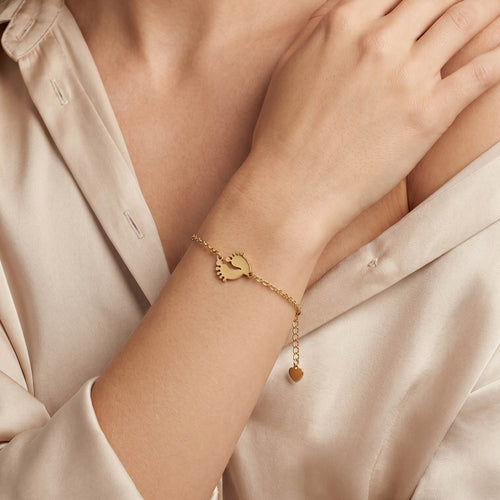 Goldfarbenes Damen Armband mit Babyfüße Anhänger am Handgelenk eines Models getragen.