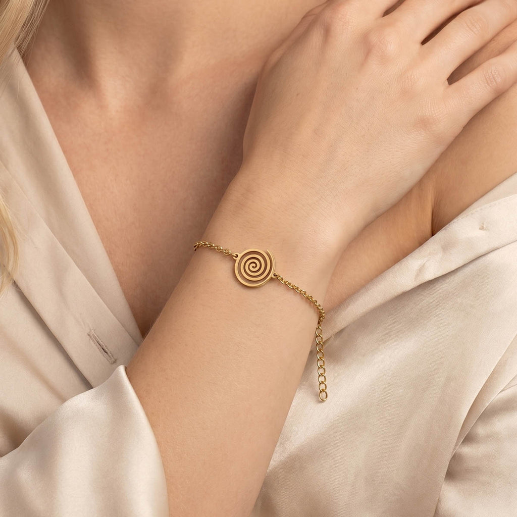 Goldfarbenes Damen Armband mit Spiralen Anhänger am Handgelenk eines Models getragen.