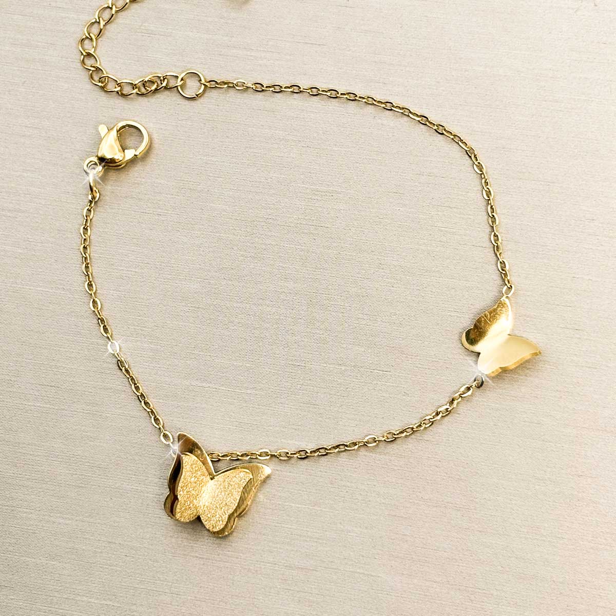 Goldfarbenes Damen-Armband aus Edelstahl mit zwei filigranen Schmetterlings-Anhängern im minimalistischen Look, Produktfoto.