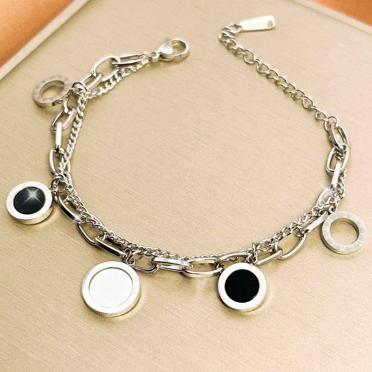 Silberfarbenes Damen-Armband aus Edelstahl im mehrlagigen Design mit runden Anhängern in kontrastierender schwarzer und silberfarbener Optik, Produktfoto