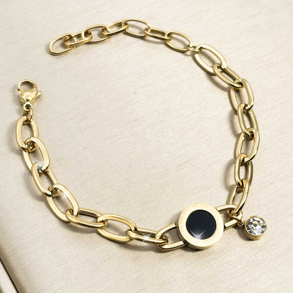 Goldfarbenes Damen-Armband aus Edelstahl mit weiten Kettengliedern, einer runden, schwarzen Einlage und einem hängenden Zirkonia-Stein, Nahaufnahme.