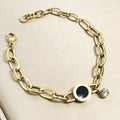 Goldfarbenes Damen-Armband aus Edelstahl mit weiten Kettengliedern, einer runden, schwarzen Einlage und einem hängenden Zirkonia-Stein, Nahaufnahme.