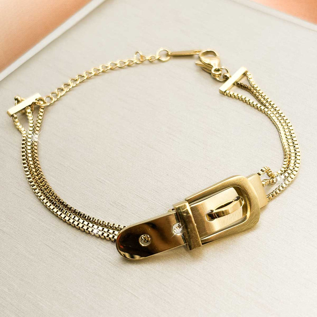 Goldfarbenes Edelstahl-Armband für Damen aus mehreren feinen Kettensträngen und einem auffälligen Element im Design einer Gürtelschnalle, Produktbild.