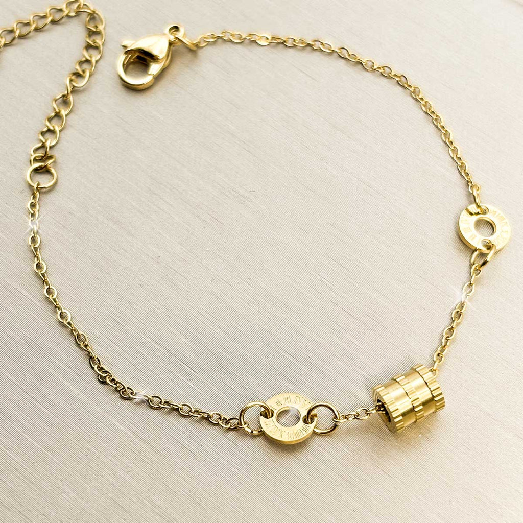 Goldfarbenes Damen-Armband aus Edelstahl mit kleinen Logoringen und einem strukturierten, kleinen Zylinder-Element, Vorderansicht.