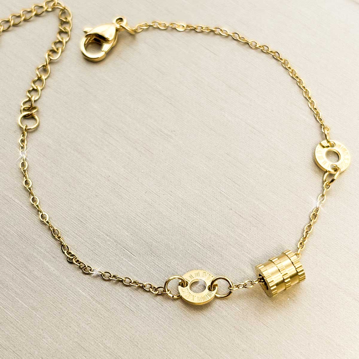 Goldfarbenes Damen-Armband aus Edelstahl mit kleinen Logoringen und einem strukturierten, kleinen Zylinder-Element, Vorderansicht.