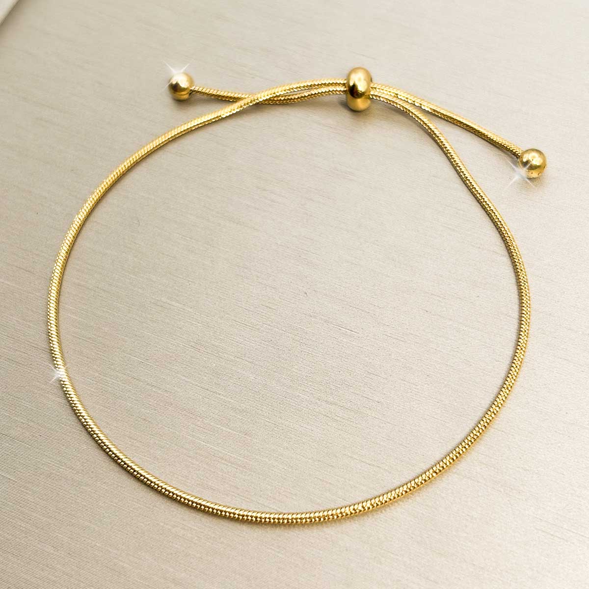 Goldfarbenes Damen-Armband aus Edelstahl im minimalistischen, glatten Schlangenketten-Design mit praktischem Zugverschluss, Produktfoto.