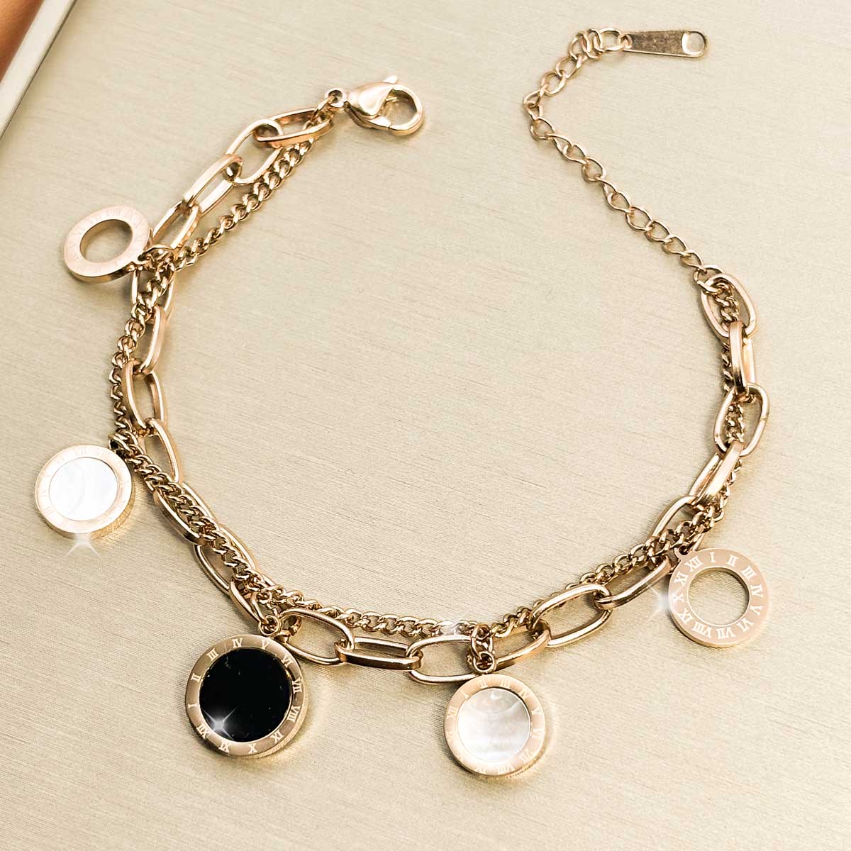 Goldfarbenes Edelstahl-Armband für Damen mit mehreren Kettensträngen und runden Anhängern in schwarzer und weißer Optik, Produktbild.