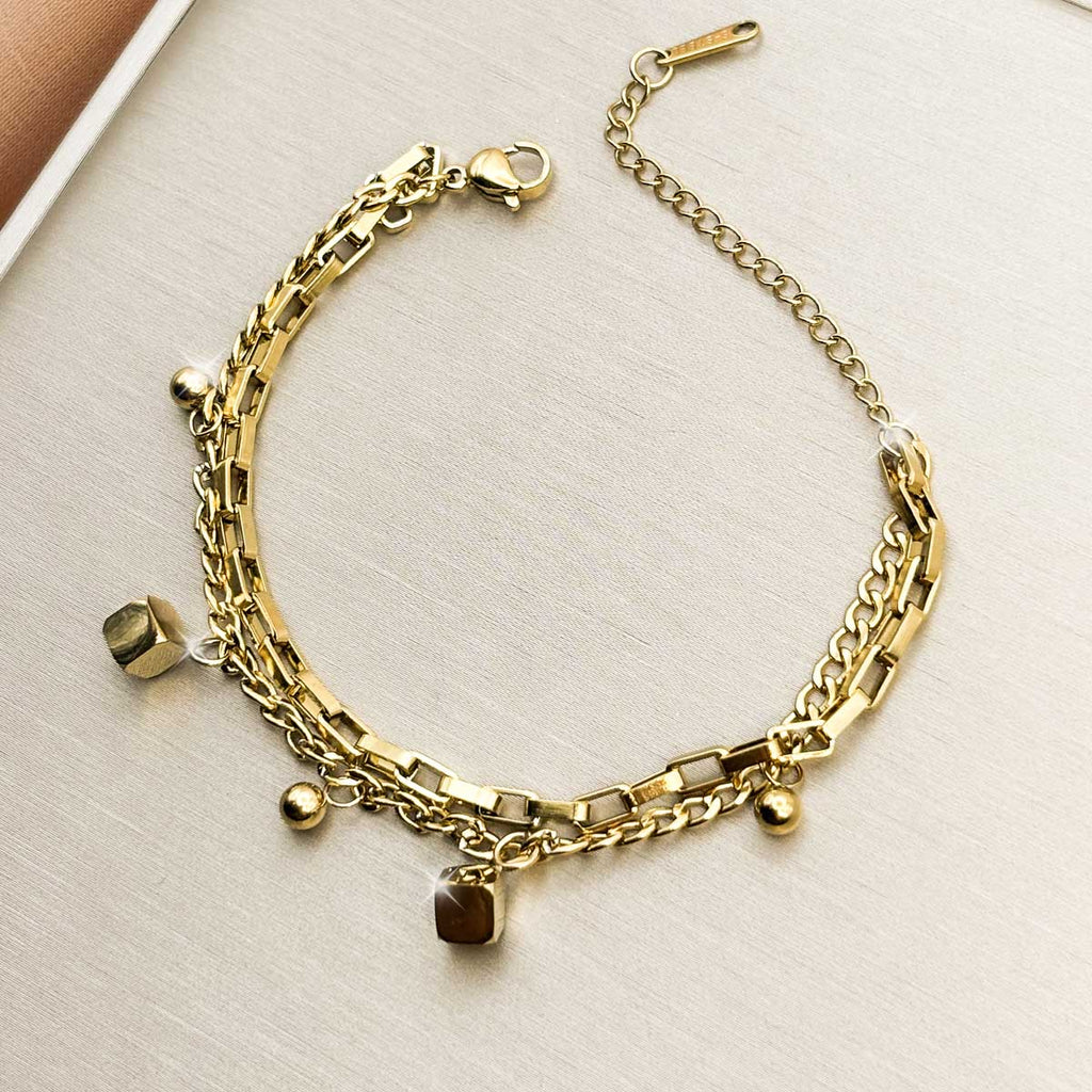 Goldfarbenes Damen-Armband aus Edelstahl im mehrlagigen Glieder-Design mit kleinen Würfel- und Kugel-Anhängern, Detail-Aufnahme.