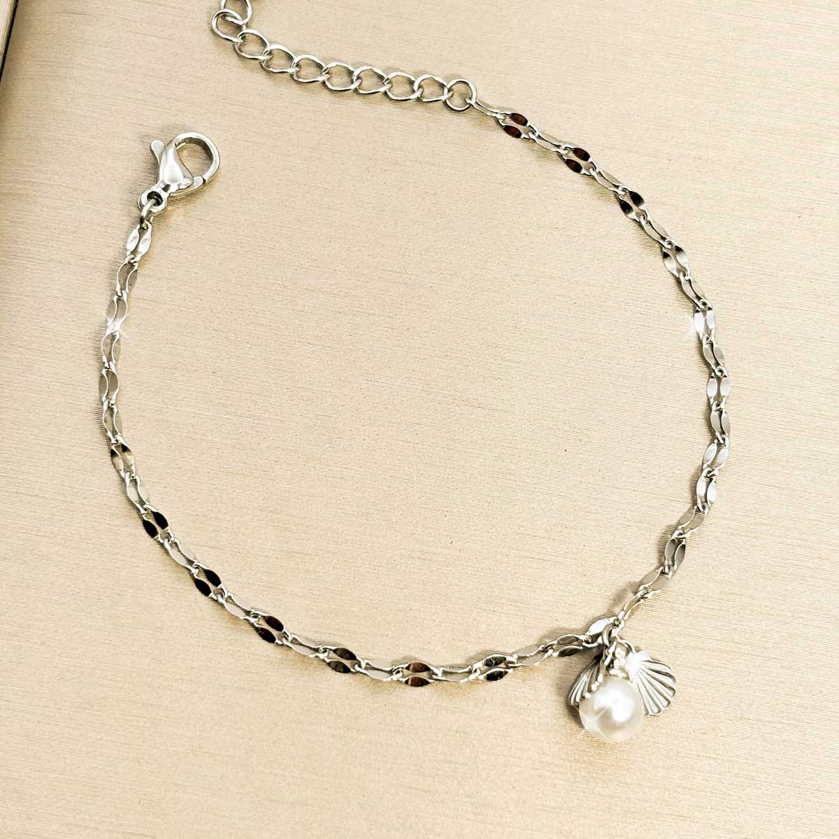 Silberfarbenes Damen-Armband aus Edelstahl mit kleinen, gedrehten Kettengliedern sowie einer weißen Perle und einem Muschel-Anhänger, Produktfoto
