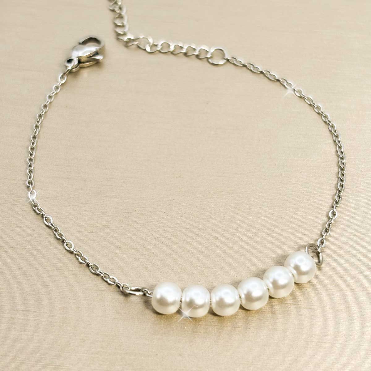 Silberfarbenes Damen-Armband aus Edelstahl mit fünf nebeneinander aufgereihten, weißen Perlen im Zentrum, Produktfoto