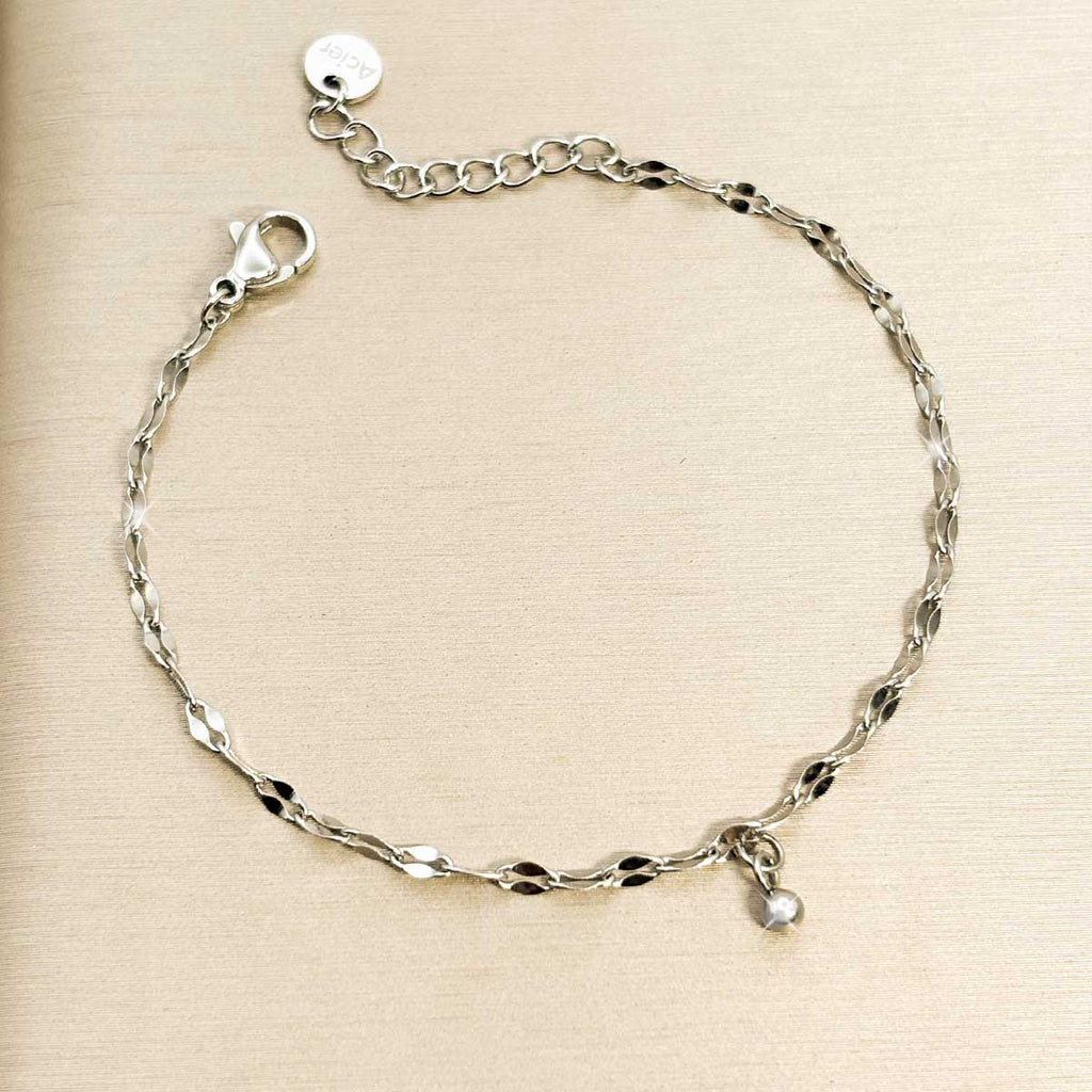 Silberfarbenes Edelstahl-Armband für Damen mit filigran gedrehten Kettengliedern und einem winzigen Tropfen-Charm, Studioaufnahme.