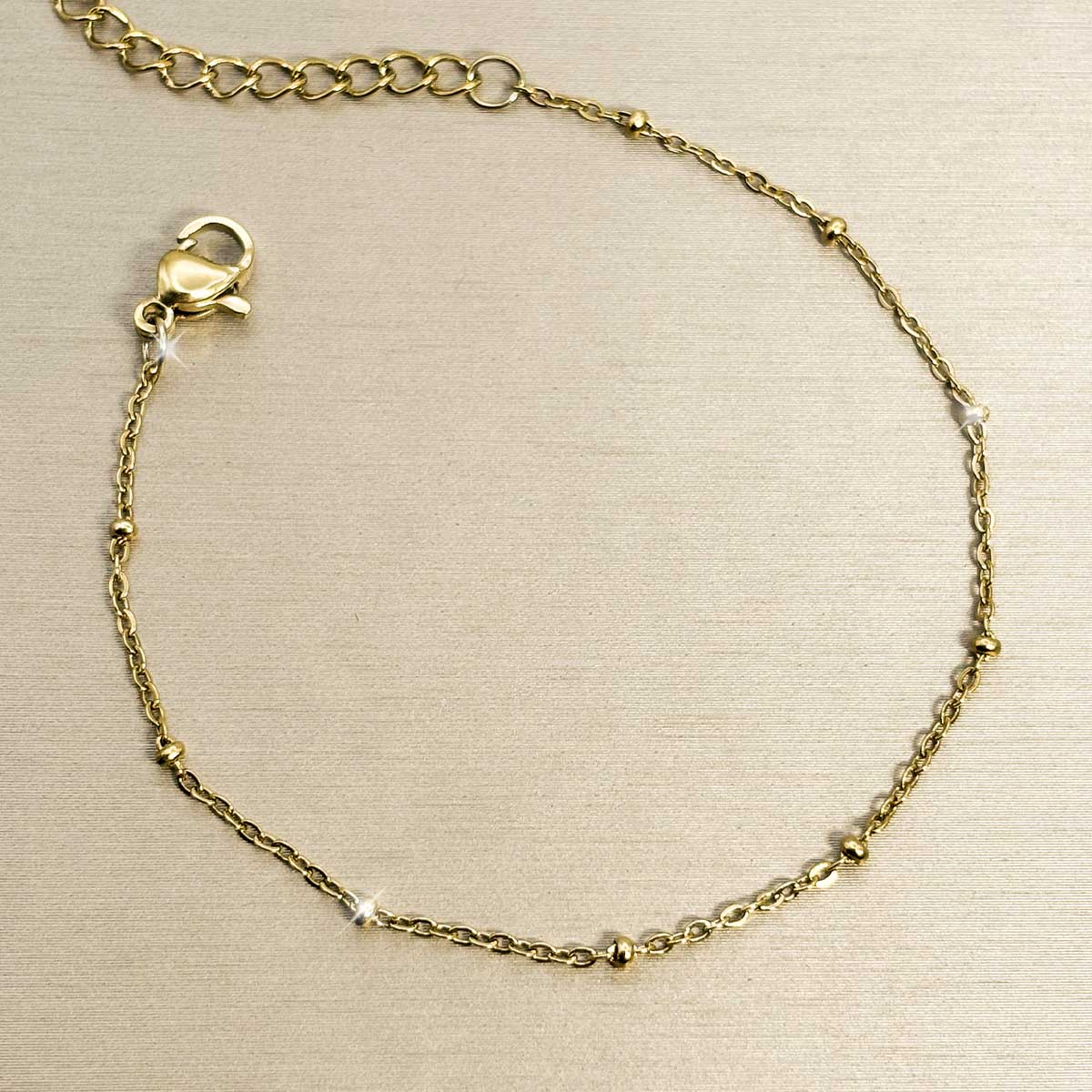 Filigranes goldfarbenes Edelstahl-Armband für Damen, dezent besetzt mit winzigen, gleichmäßig verteilten Kügelchen, Produktbild.