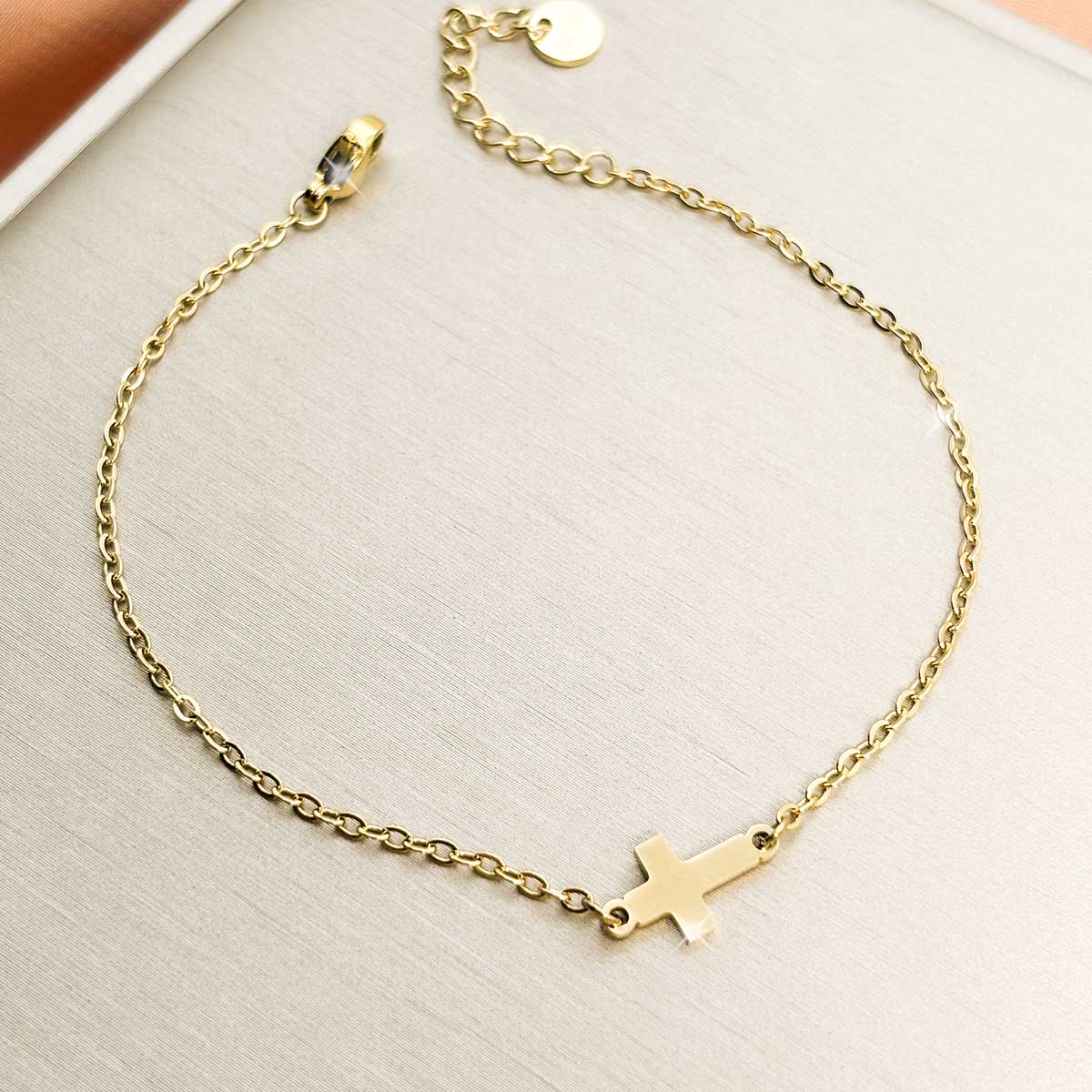 Goldfarbenes Damen-Armband aus Edelstahl mit einem dezenten, horizontal integrierten Kreuz-Anhänger, Produktfoto.