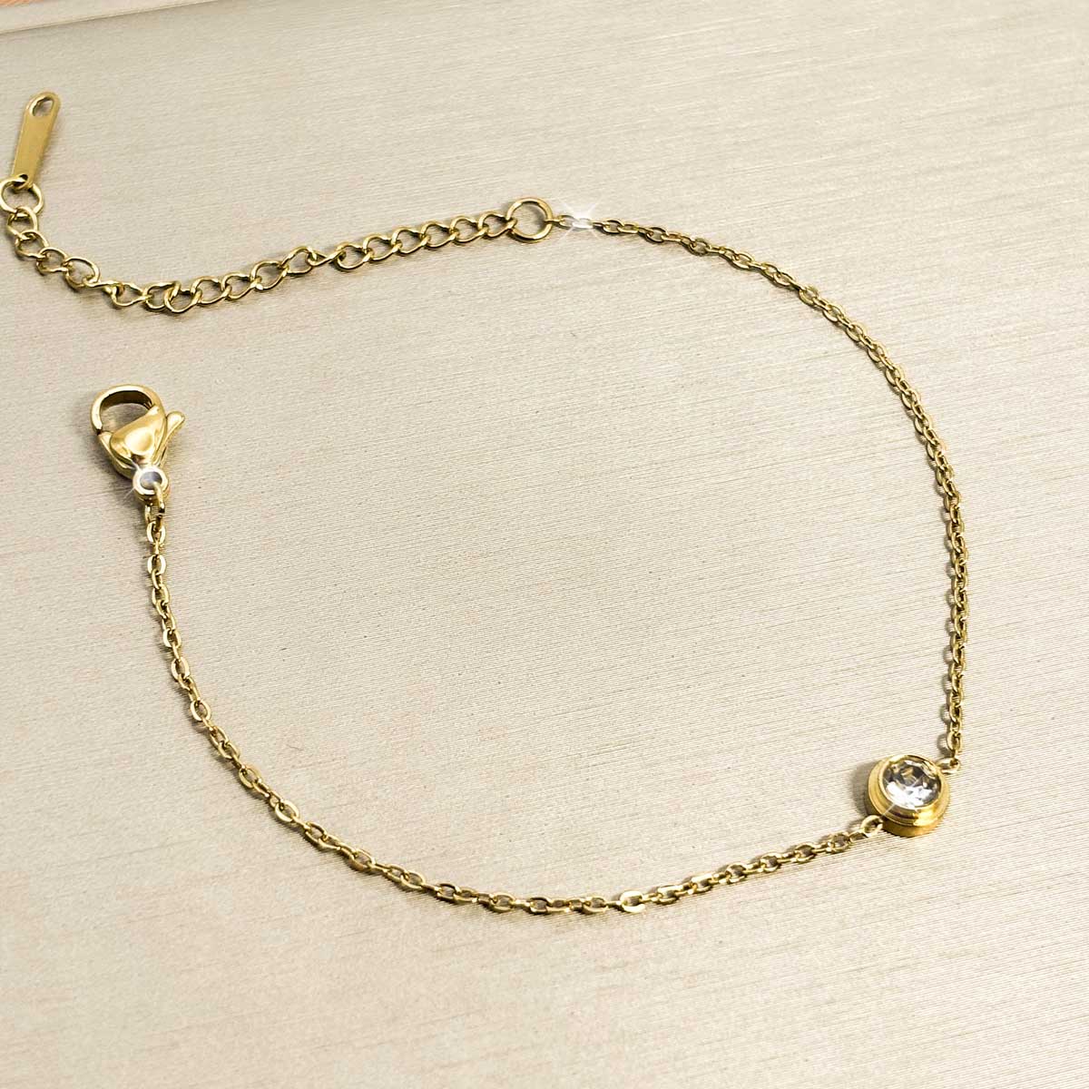 Goldfarbenes Edelstahl-Armband für Damen mit einem kleinen, rund gefassten Zirkonia-Solitär als Zwischenelement, Studioaufnahme.