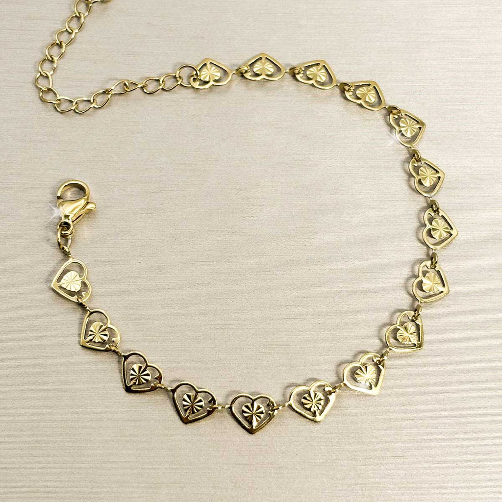 Goldfarbenes Damen-Armband aus Edelstahl, zusammengesetzt aus einer Reihe kleiner, filigran gemusterter Herz-Glieder, Produktfoto