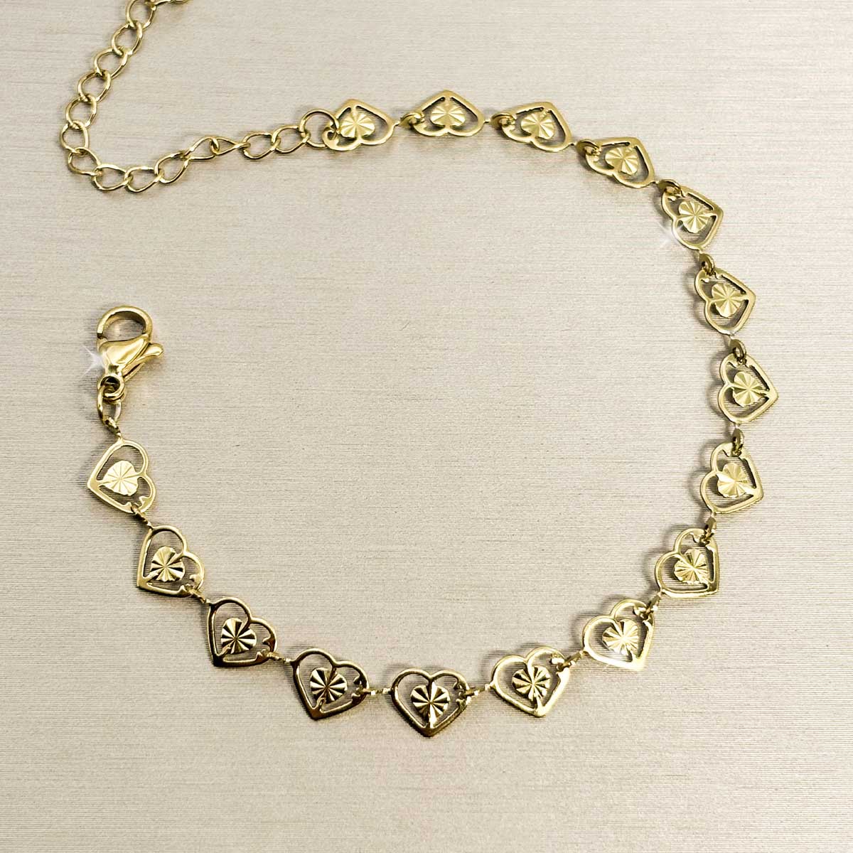 Goldfarbenes Damen-Armband aus Edelstahl, zusammengesetzt aus einer Reihe kleiner, filigran gemusterter Herz-Glieder, Produktfoto