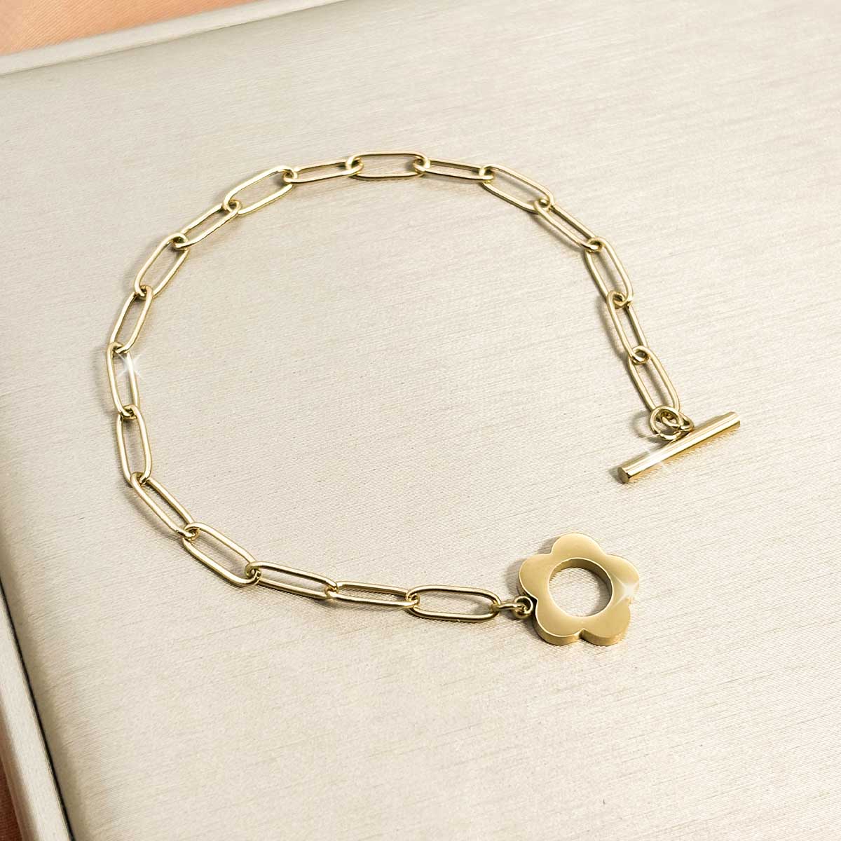 Goldfarbenes Damen-Armband aus Edelstahl mit länglichen Kettengliedern und einem dekorativen Knebelverschluss in Blumen-Form, Nahaufnahme.