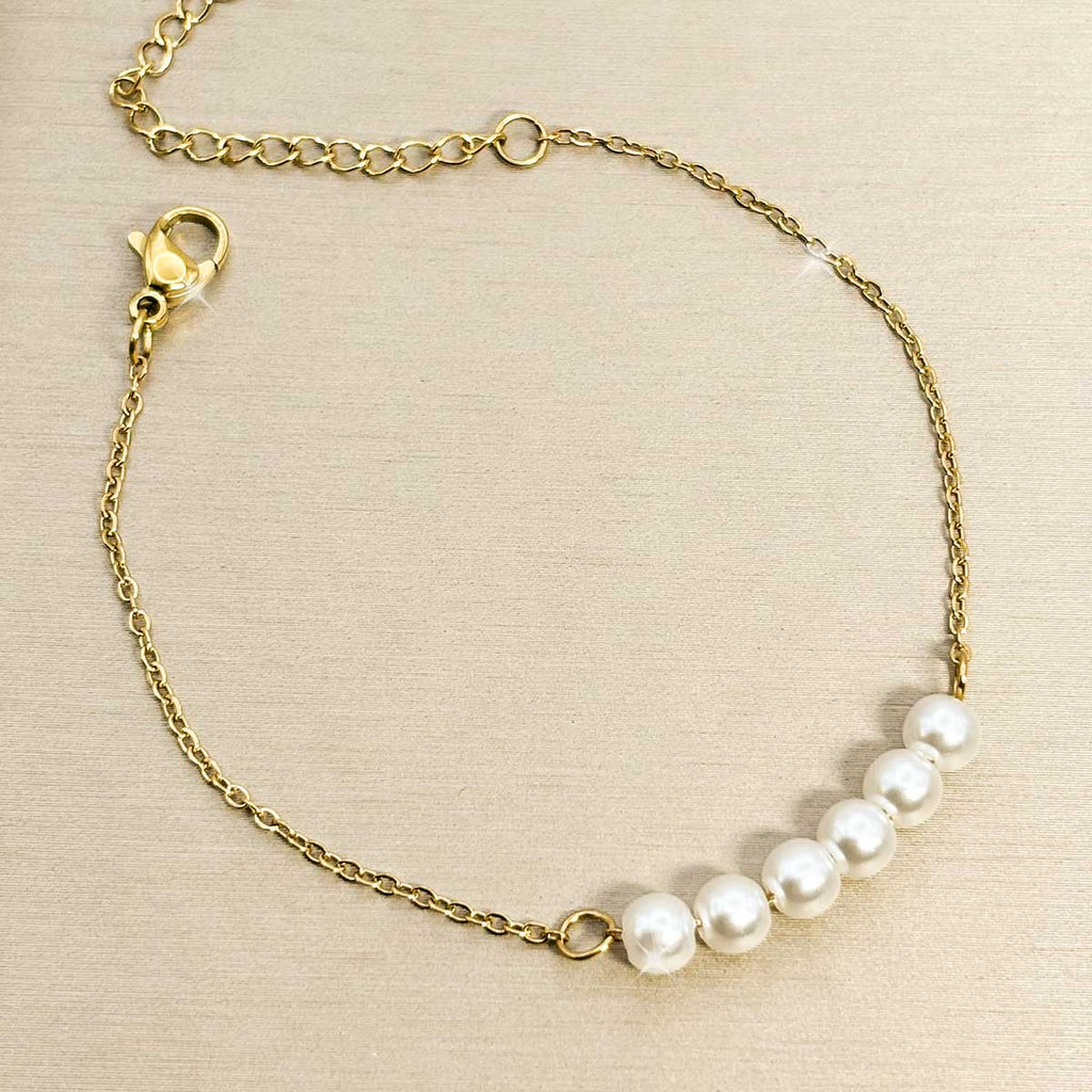 Goldfarbenes Edelstahl-Armband für Damen mit fünf nebeneinander aufgereihten, weißen Perlen im Zentrum, Produktbild.