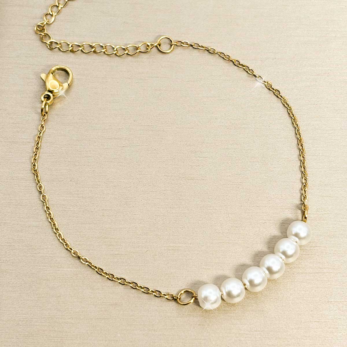 Goldfarbenes Edelstahl-Armband für Damen mit fünf nebeneinander aufgereihten, weißen Perlen im Zentrum, Produktbild.