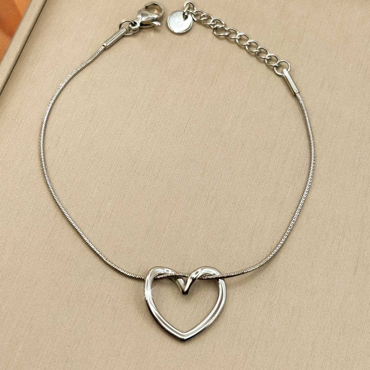 Silberfarbenes Damen-Armband aus Edelstahl mit einem elegant geschwungenen Herz-Anhänger, Nahaufnahme.