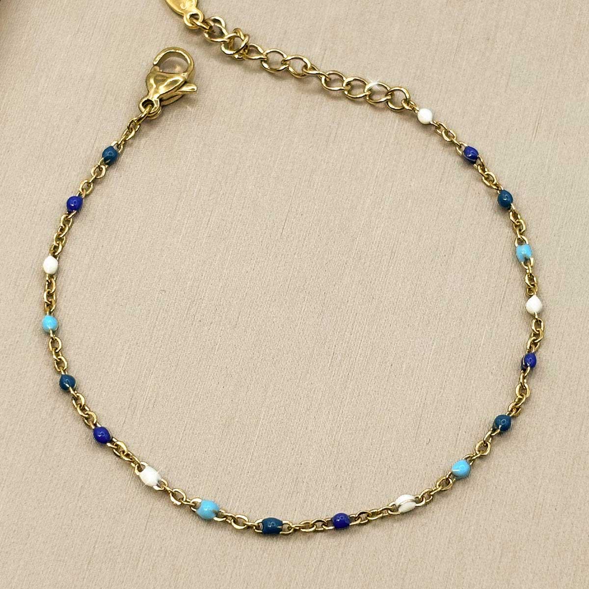 Filigranes goldfarbenes Damen-Armband aus Edelstahl, besetzt mit kleinen blau-weißen Perlen-Akzenten, Vorderansicht.