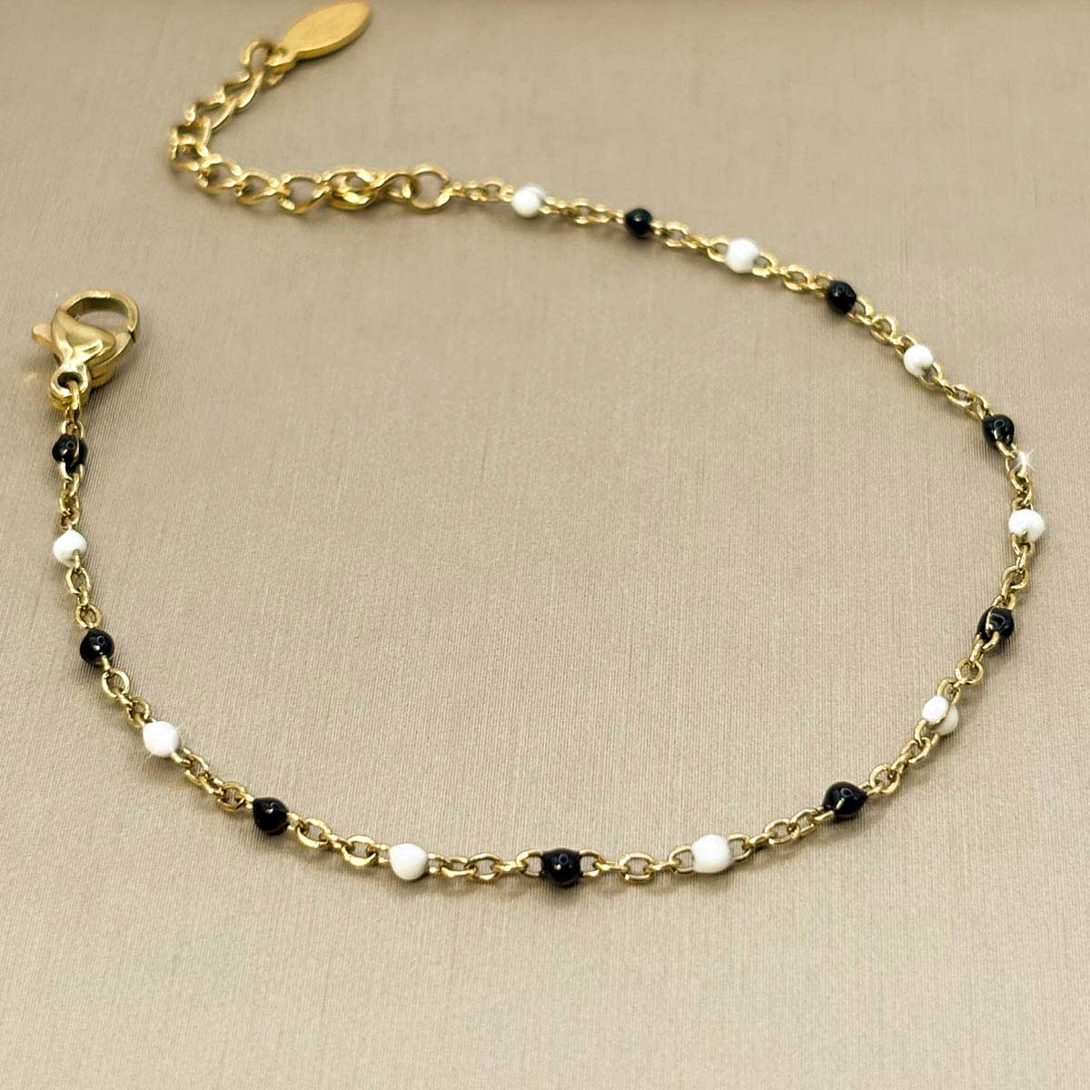 Filigranes goldfarbenes Damen-Armband aus Edelstahl, besetzt mit kleinen schwarz-weißen Perlen-Akzenten, Nahaufnahme.