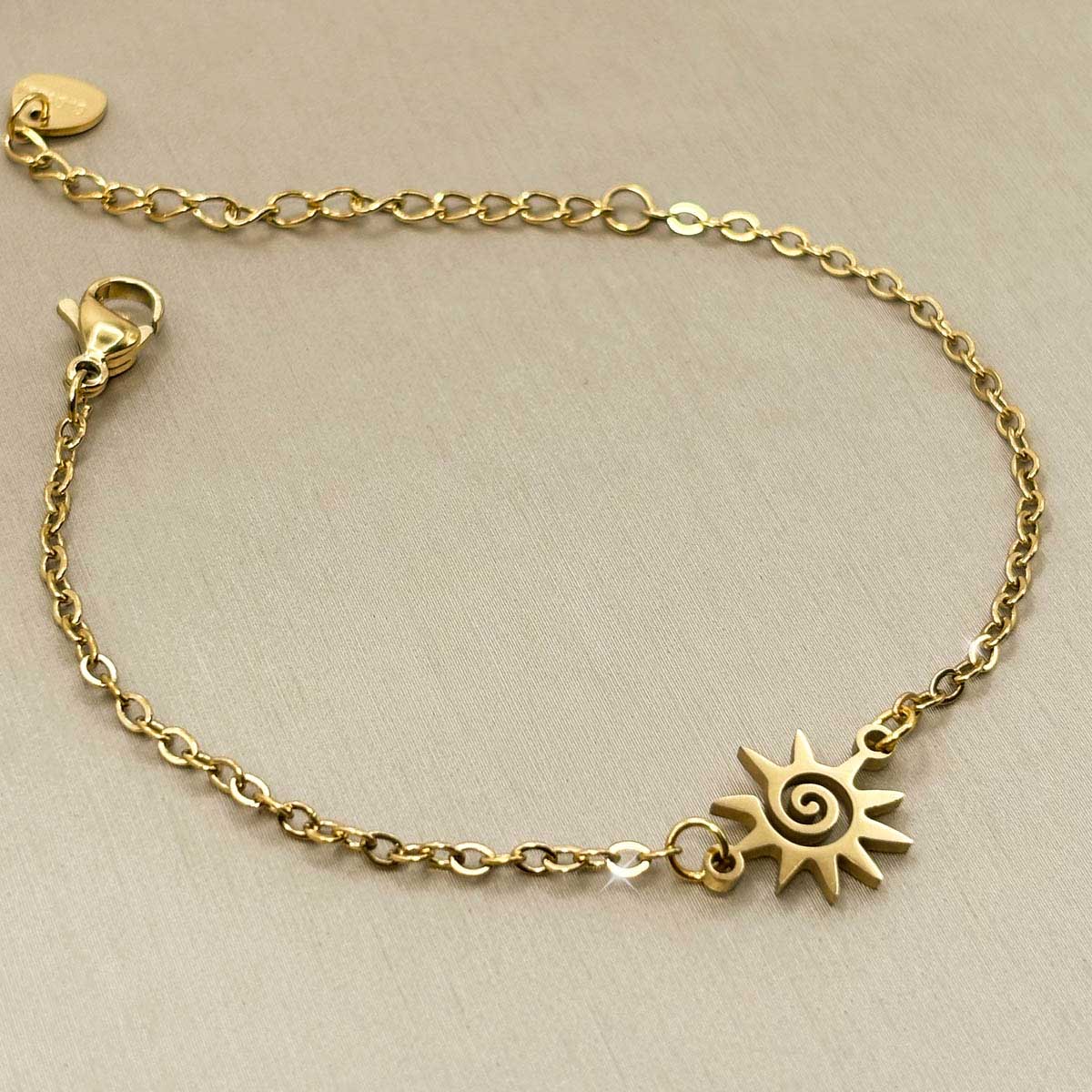 Goldfarbenes Edelstahl-Armband für Damen mit einem verspielten Sonnen-Element samt integrierter Spirale, Studioaufnahme.