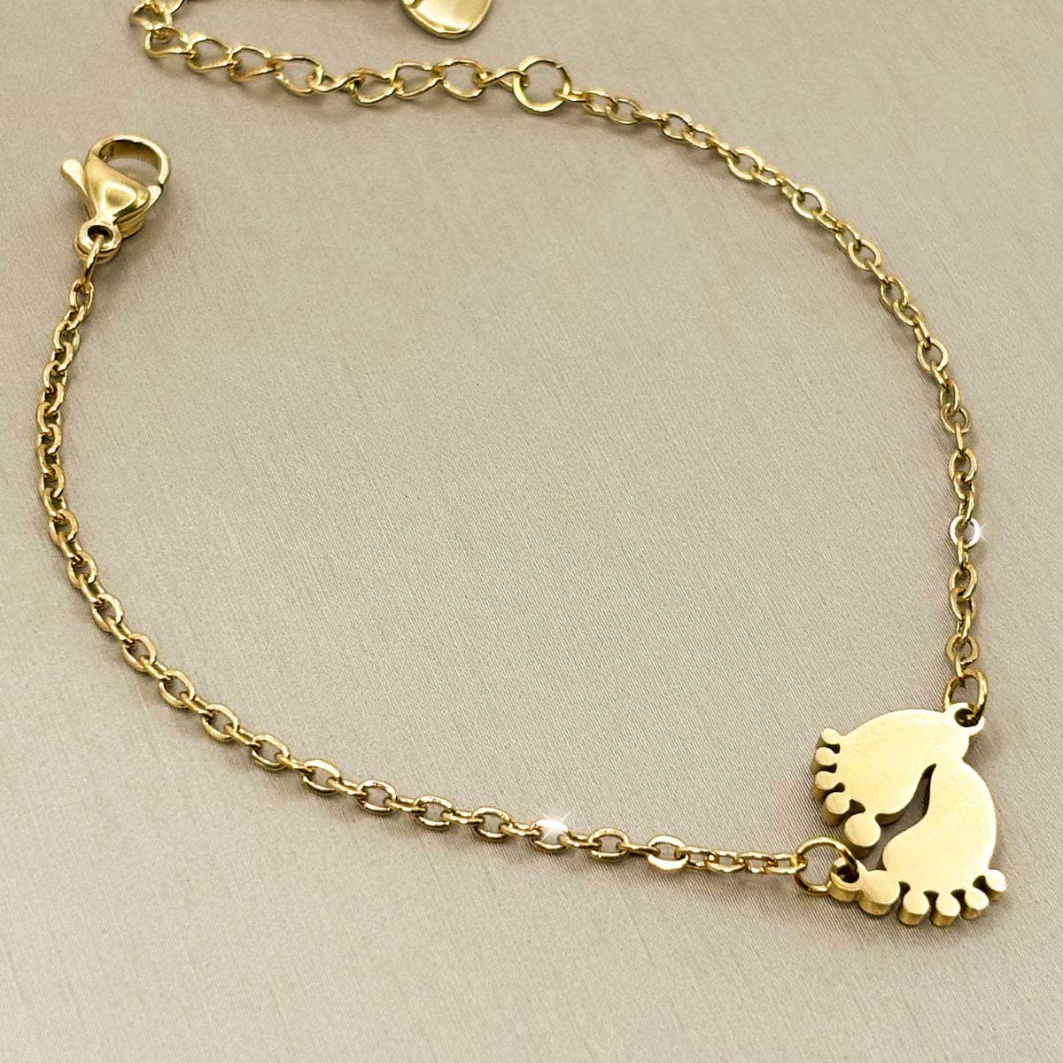Goldfarbenes Damen-Armband aus Edelstahl mit zwei kleinen, niedlichen Babyfuß-Anhängern, Nahaufnahme.