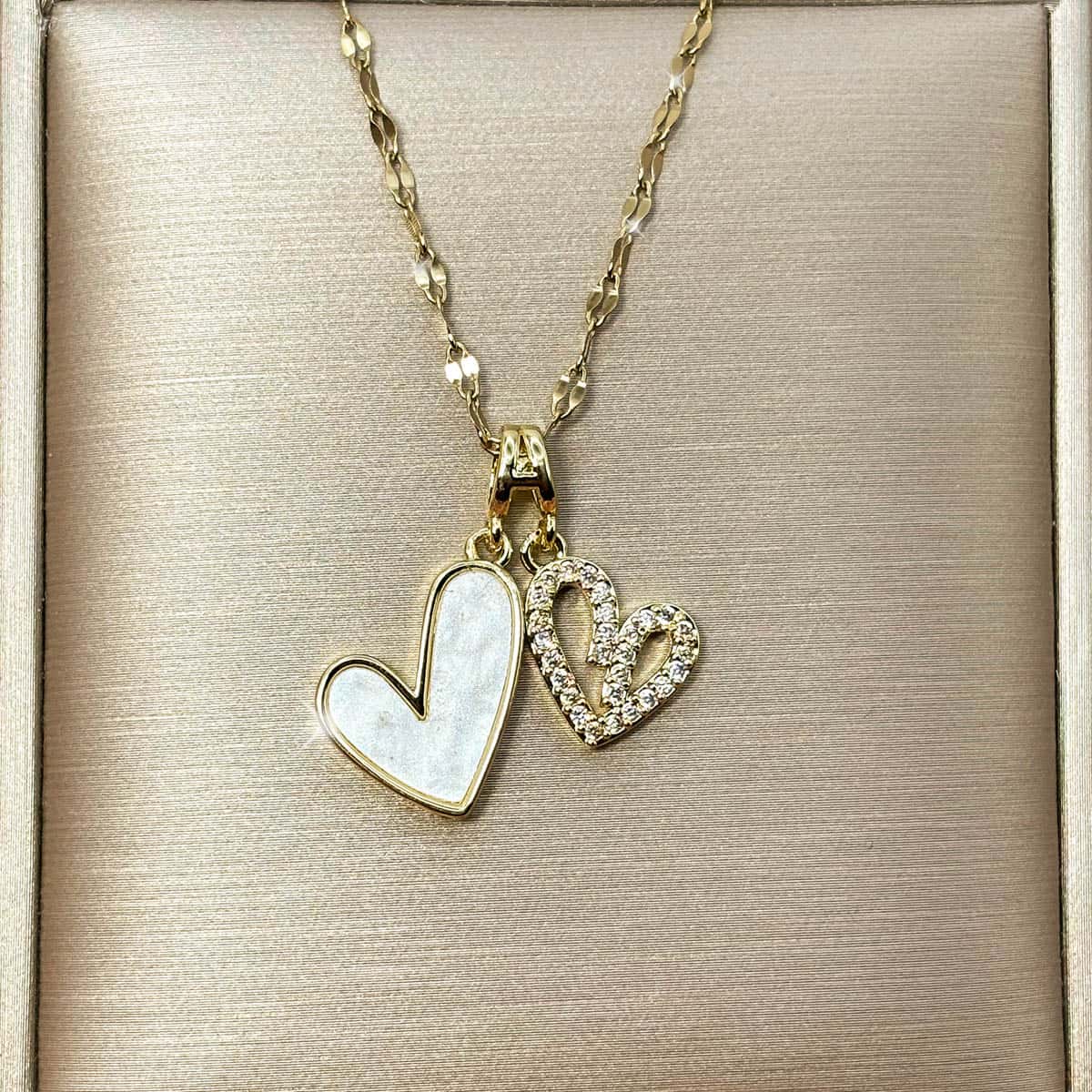 Damen Halskette mit zwei Herz-Anhängern, ein Herz in edler Perlmutt-Optik und ein Herz im Cut-Out-Design mit glitzerndem Zirkonia Besatz, Nahaufnahme der Vorderseite.