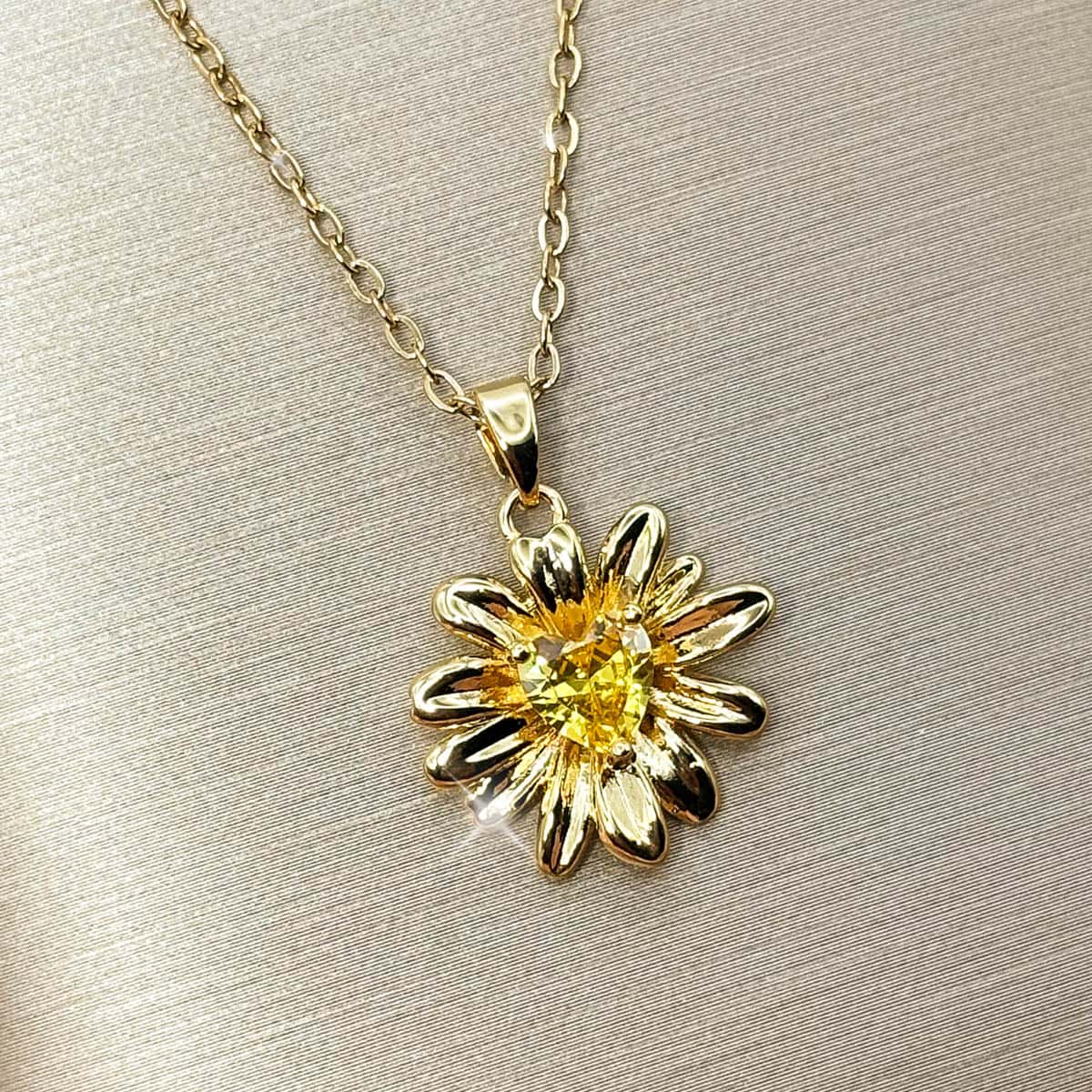 Halskette mit detailreichem Sonnenblumen-Anhänger und einem leuchtend gelben Zirkonia-Stein im Zentrum, Studio-Produktfoto von links.