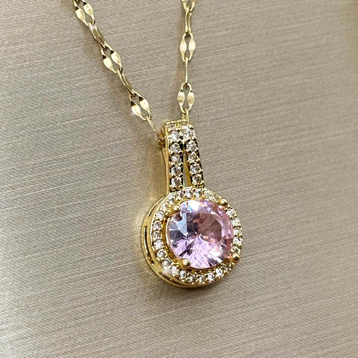 Halskette mit kreisrundem Anhänger, einem großen rosa Zirkonia-Stein im Zentrum und kleiner Zirkonia-Umrandung, Nahaufnahme von links