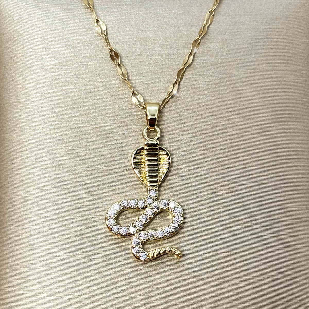 Goldene Halskette mit geschwungenem Schlangen-Anhänger im Kobra-Design, Detailaufnahme.