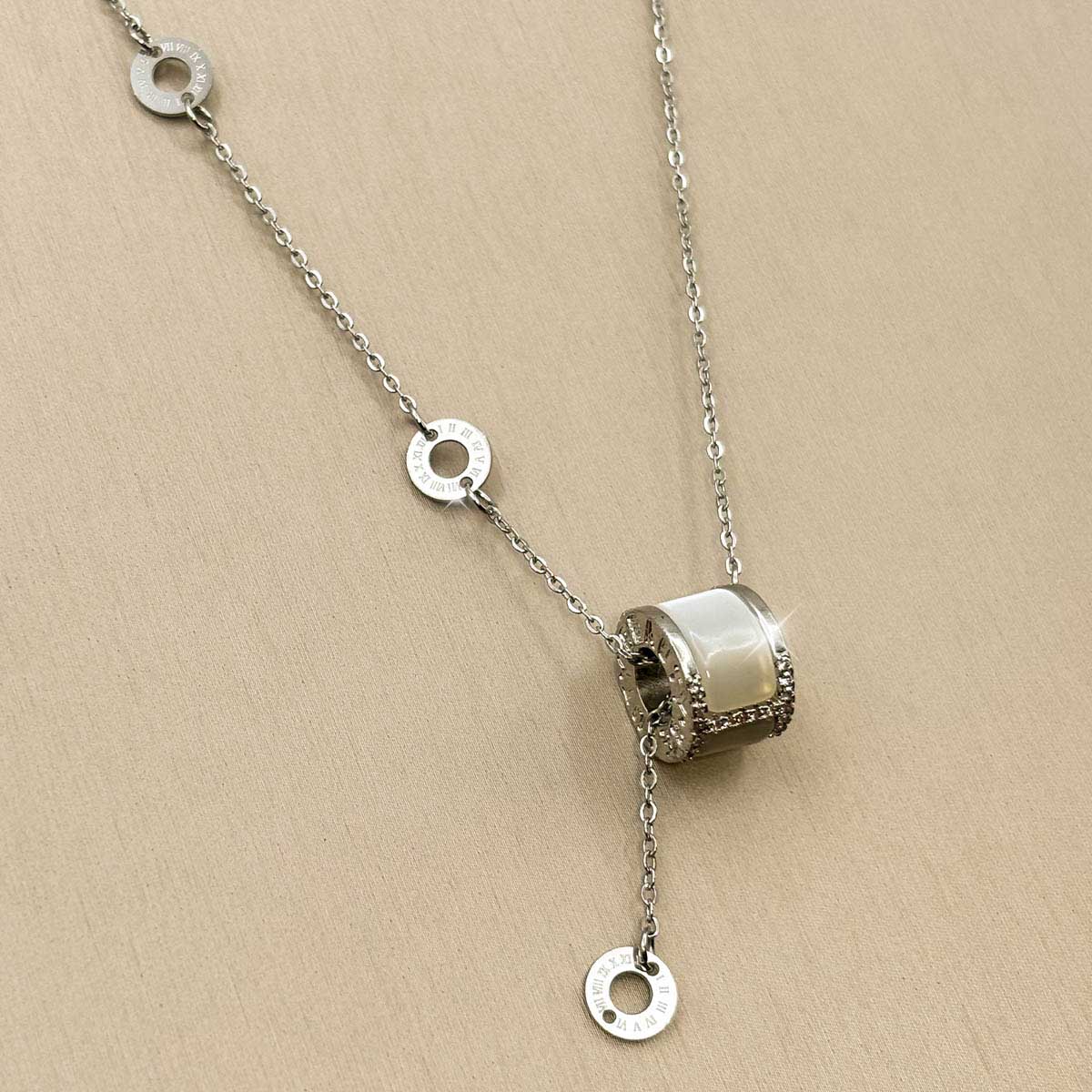 Silberfarbene Damen-Halskette aus Edelstahl im Y-Design mit kleinen Logoringen und einem zylindrischen Anhänger mit hellem Inlay, Nahaufnahme.