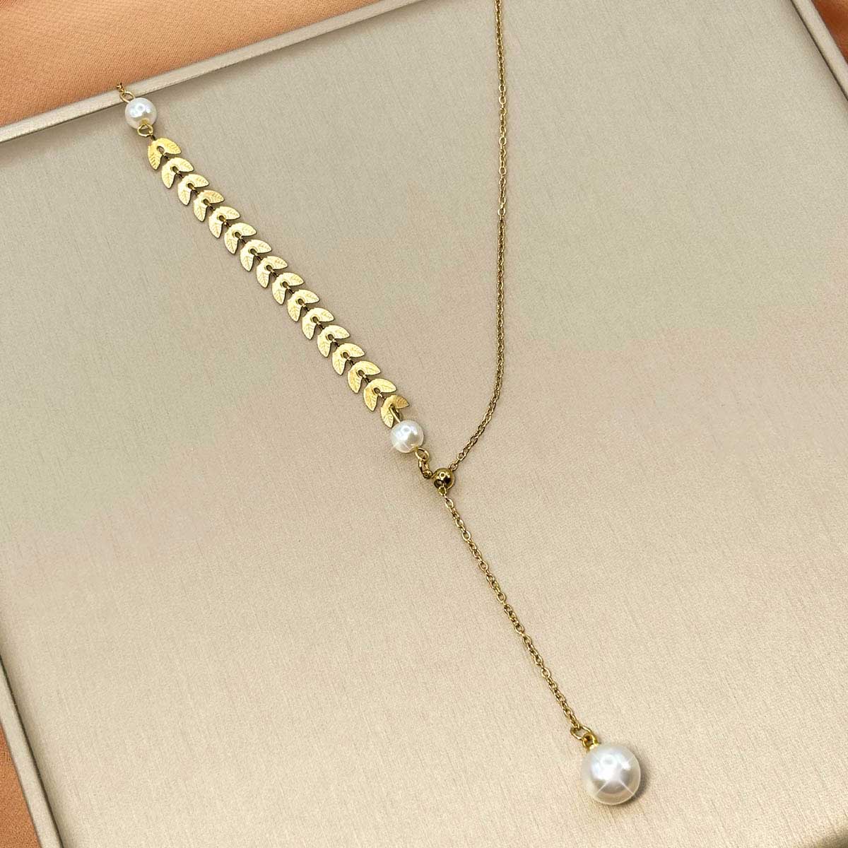 Goldfarbene Edelstahl-Halskette für Damen im asymmetrischen Y-Design mit einer feinen Perle, hängendem Kettenstrang und Ähren-Struktur, Detail-Aufnahme.