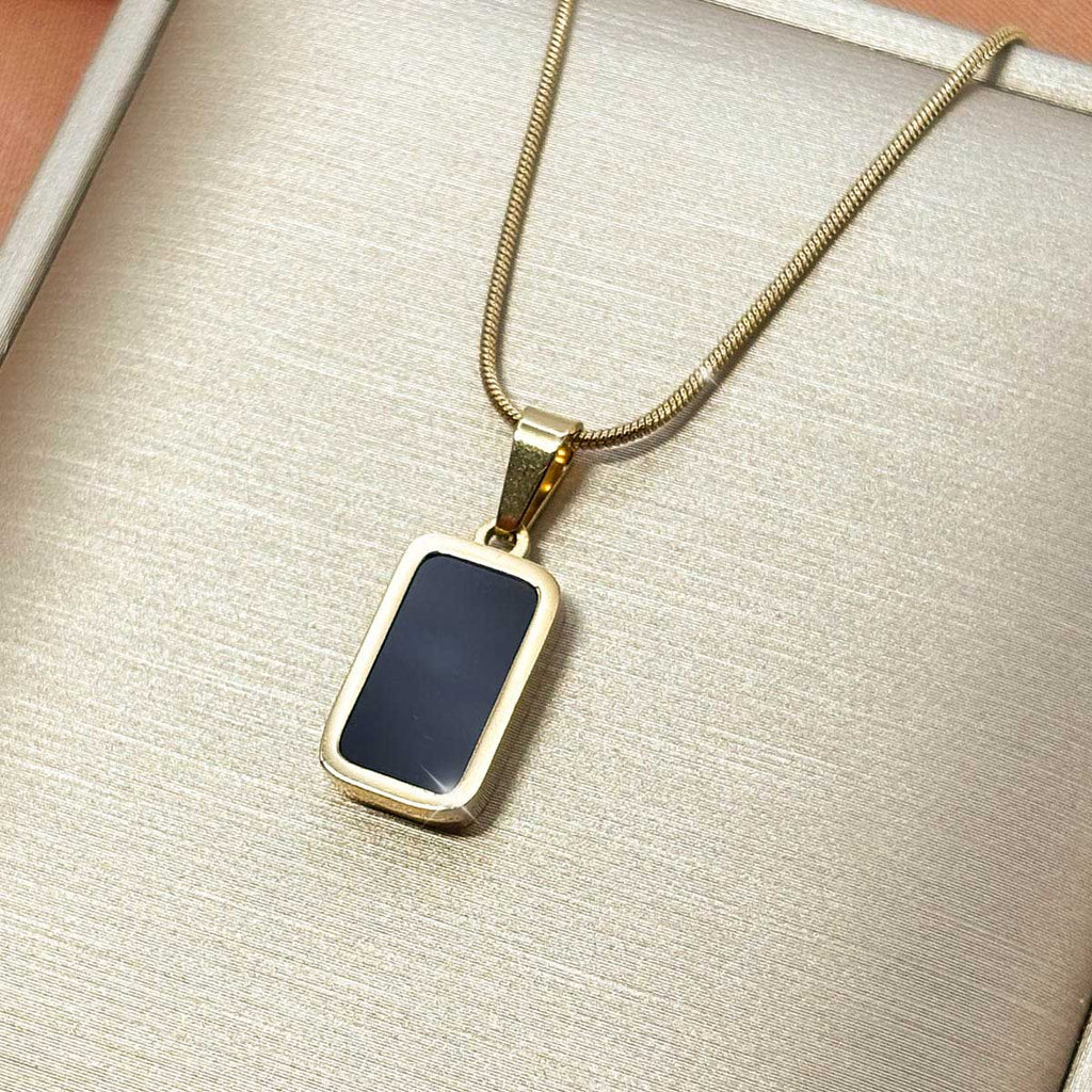 Goldfarbene Edelstahl-Halskette für Damen an feiner Schlangenkette mit einem rechteckigen Anhänger in schwarzer Onyx-Optik, Studioaufnahme.
