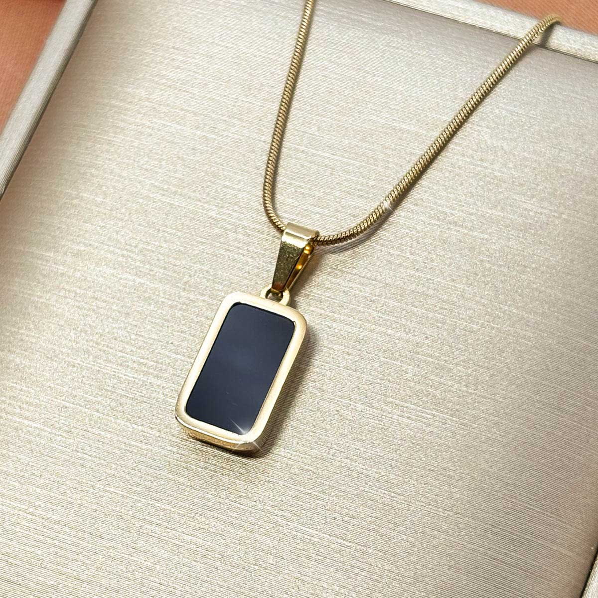 Goldfarbene Edelstahl-Halskette für Damen an feiner Schlangenkette mit einem rechteckigen Anhänger in schwarzer Onyx-Optik, Studioaufnahme.