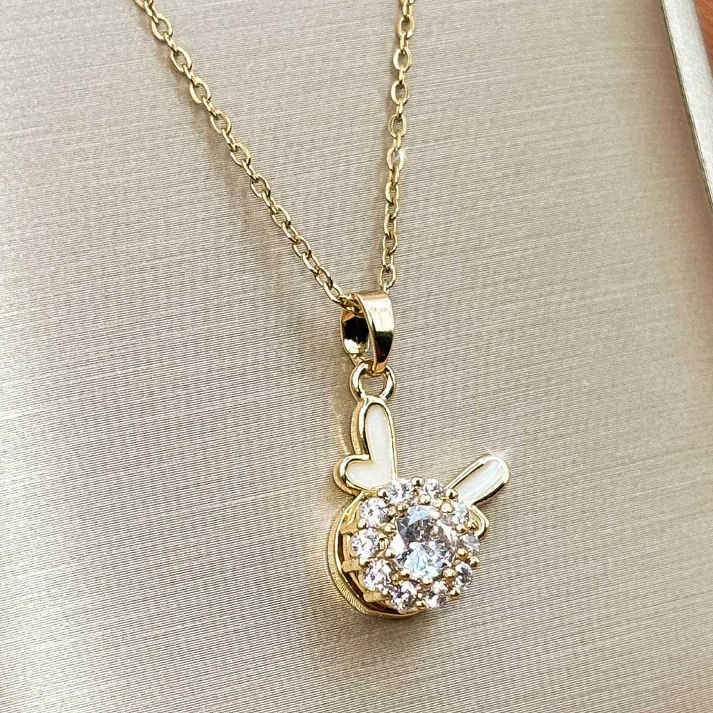 Goldfarbene Edelstahl-Halskette für Damen mit einem runden Solitär-Zirkonia-Anhänger und minimalistischen Hasenohren-Details, Studioaufnahme.