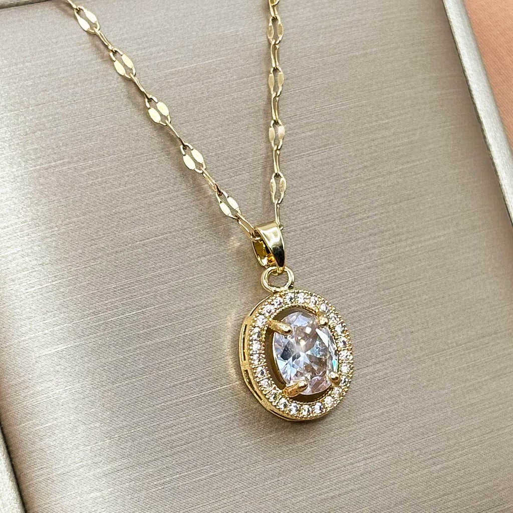 Goldfarbene Edelstahl-Halskette für Damen mit einem ovalen Halo-Anhänger, besetzt mit einem großen Zirkonia-Zentrum und funkelndem Rahmen, Detail-Aufnahme.