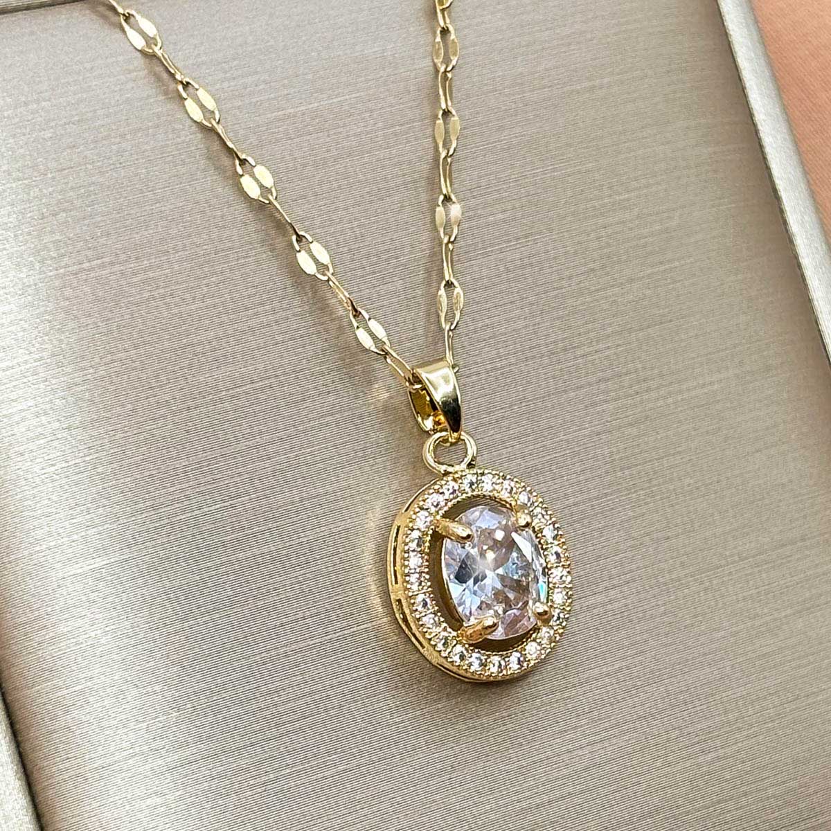 Goldfarbene Edelstahl-Halskette für Damen mit einem ovalen Halo-Anhänger, besetzt mit einem großen Zirkonia-Zentrum und funkelndem Rahmen, Detail-Aufnahme.