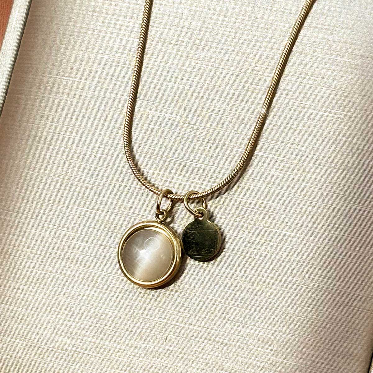 Silberfarbene Damen-Halskette aus Edelstahl an feiner Schlangenkette mit einer runden, zart schimmernden Plakette und einem kleinen Metall-Plättchen, Produktfoto