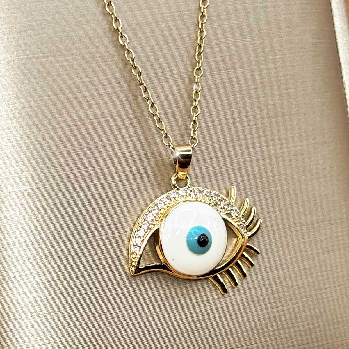 Goldfarbene Edelstahl-Halskette für Damen mit einem auffälligen Auge-Anhänger im Nazar-Design mit langen Wimpern und hellem Inlay, Studioaufnahme.