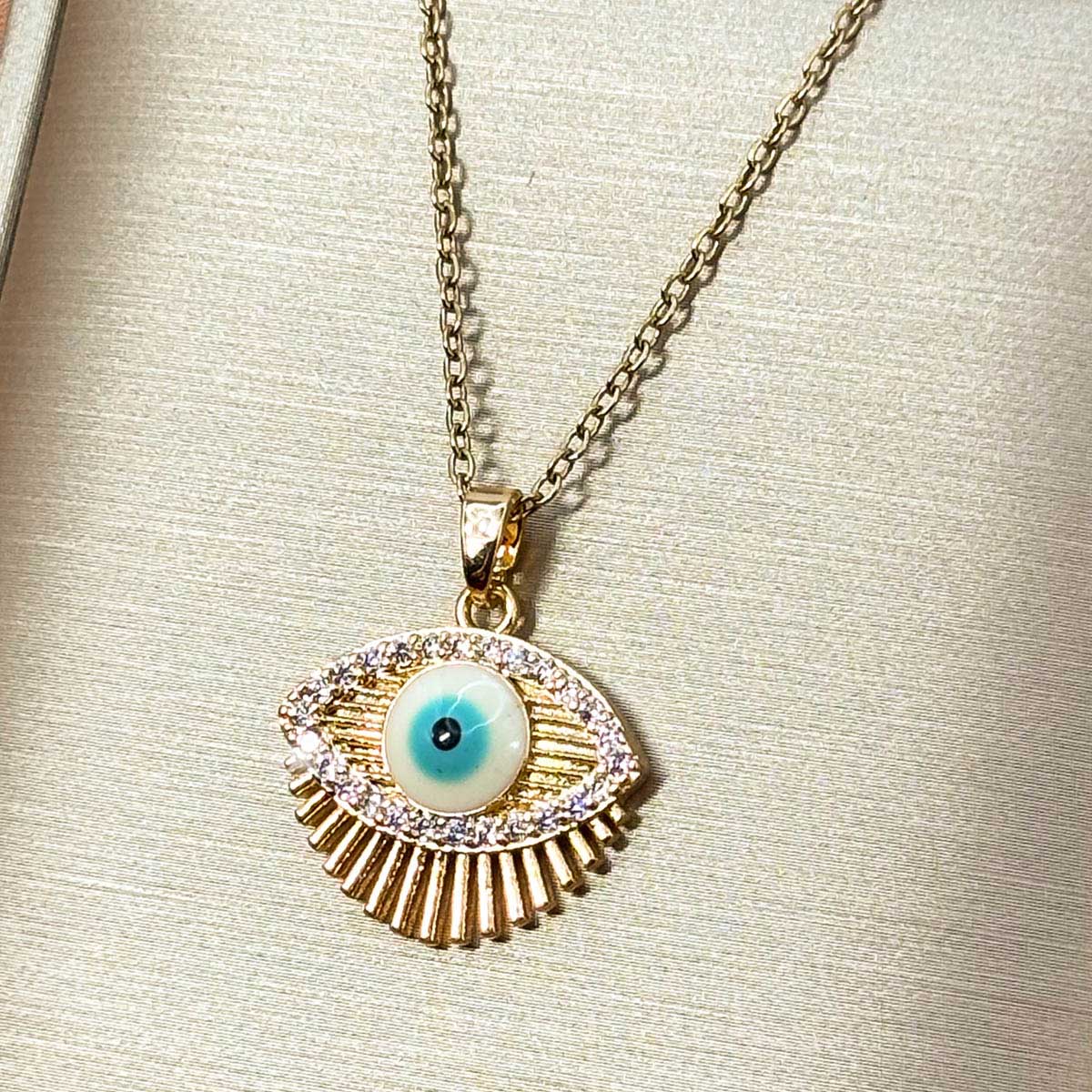 Goldfarbene Edelstahl-Halskette für Damen mit einem detaillierten Nazar-Auge-Anhänger, umrahmt von einer funkelnden Zirkonia-Spur und feinen Strahlen, Vorderansicht.