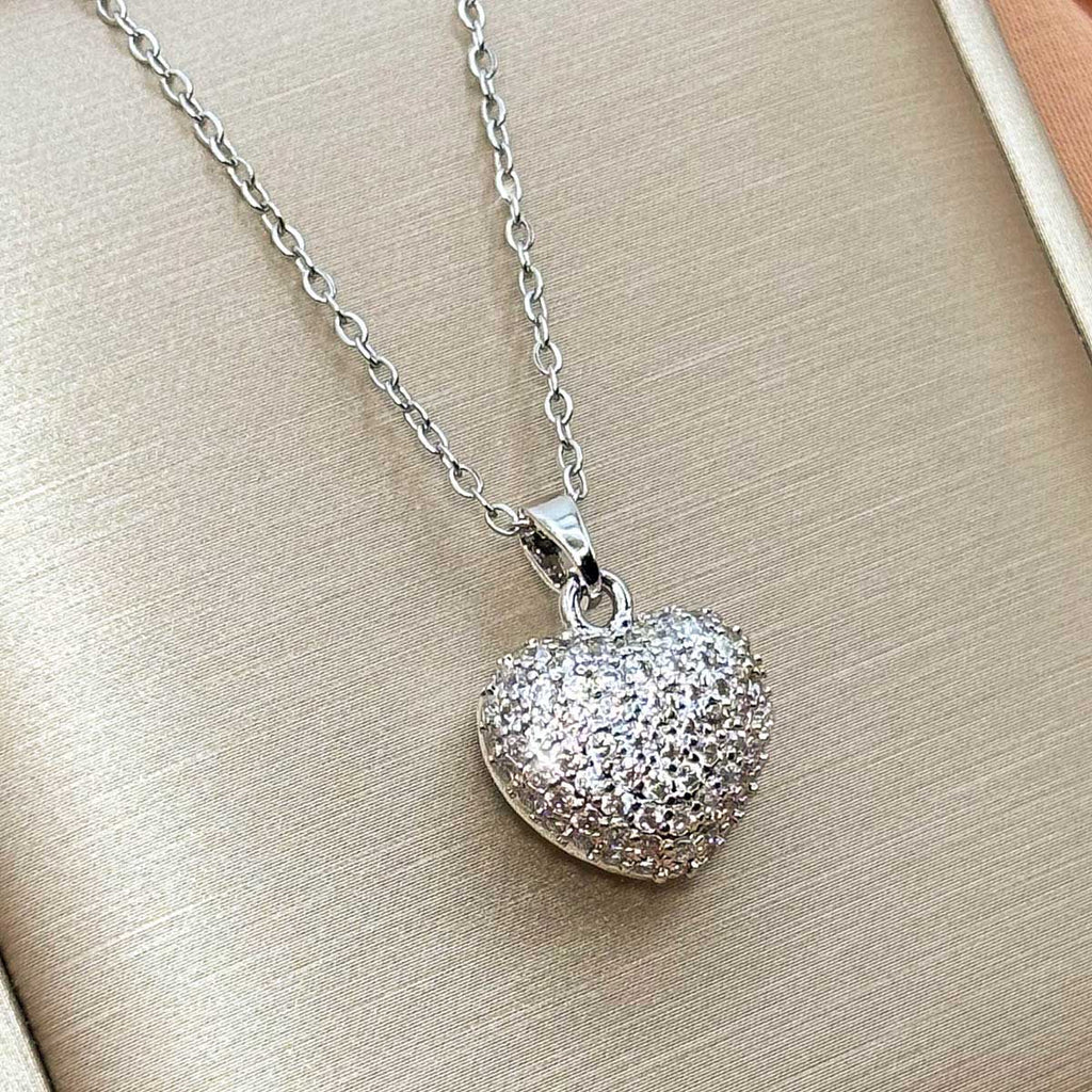 Silberfarbene Damen-Halskette aus Edelstahl mit einem bauchigen, vollflächig mit funkelnden Zirkonia besetzten Herz-Anhänger, Nahaufnahme.