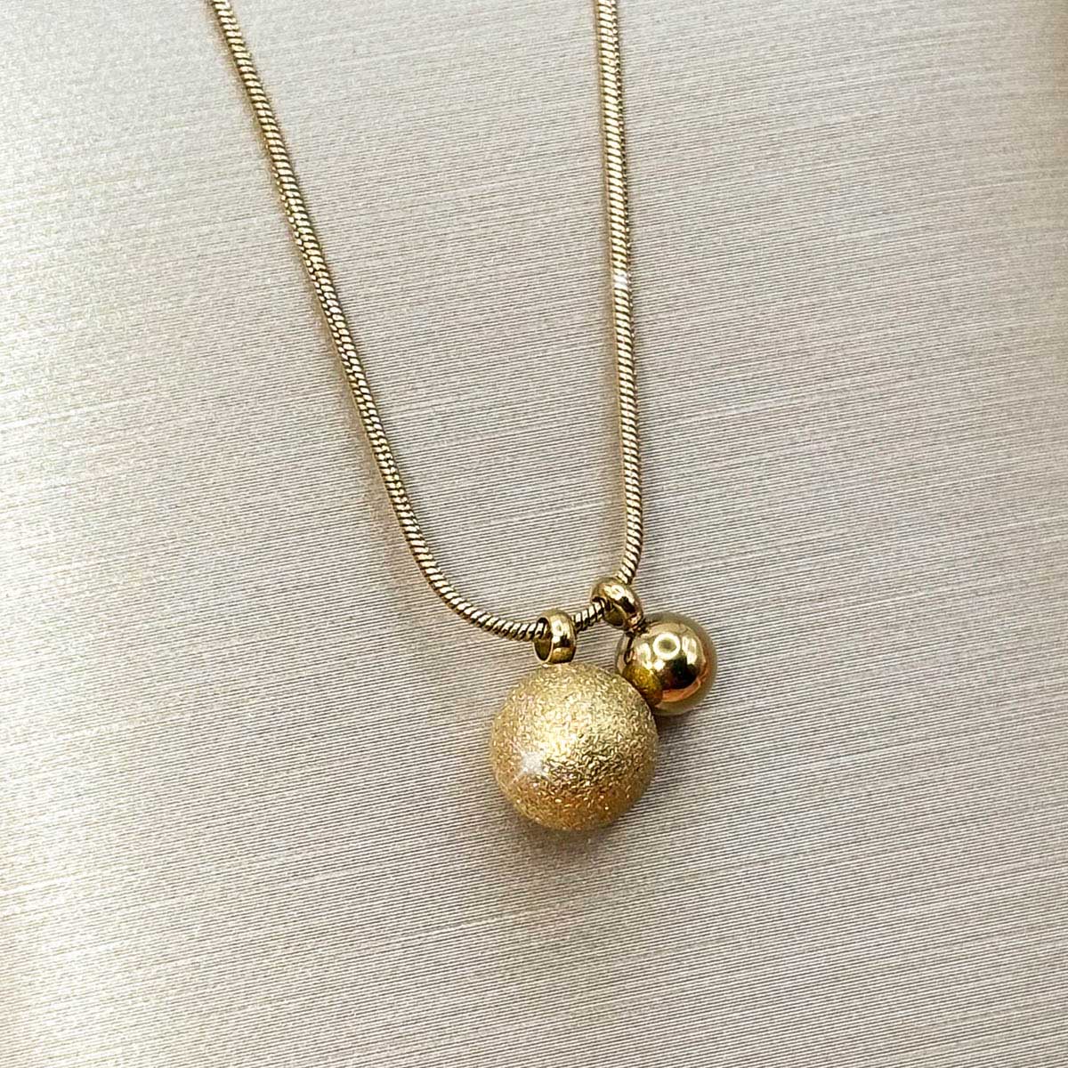 Goldfarbene Damen-Halskette aus Edelstahl an feiner Schlangenkette mit zwei unterschiedlich großen, matt strukturierten Kugeln, Produktfoto.